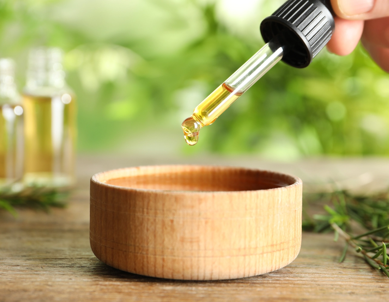 Essential Oil dropper being dropping essential oil into a wooden bowl
