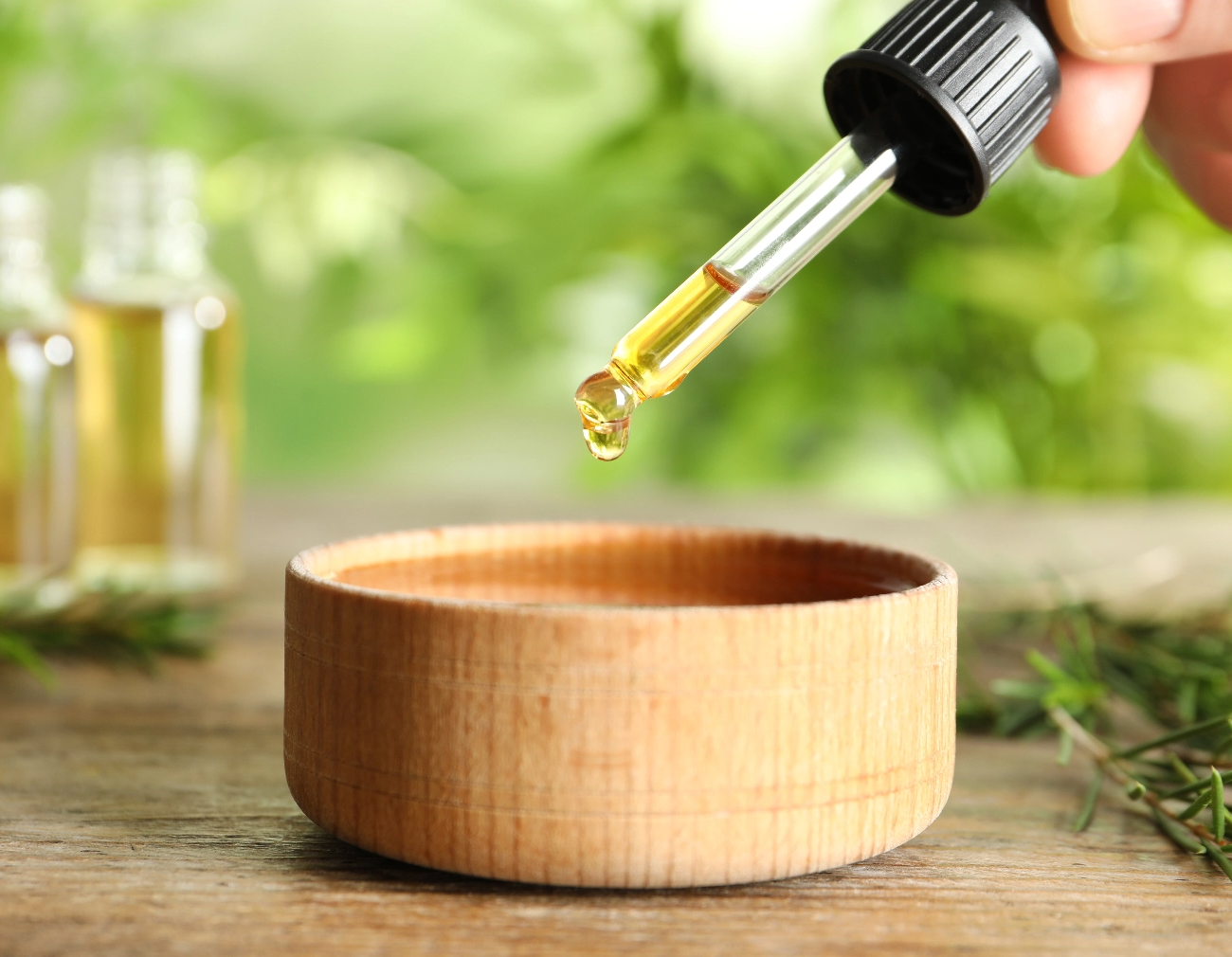 Essential Oil dropper being dropping essential oil into a wooden bowl 